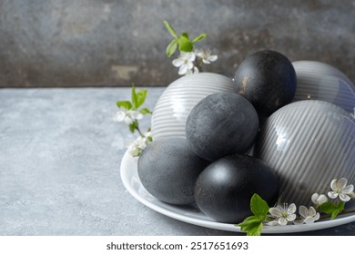 A stylish arrangement of black and white decorative eggs on a white plate, complemented by cherry blossom branch. Set against a textured background, creating a sophisticated display. - Powered by Shutterstock