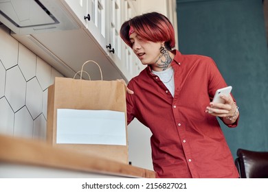 Stylish Asian Guy Holding Phone While Receiving Food Delivery At Home