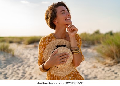 Stylish Attractive Slim Smiling Woman On Beach In Summer Style Fashion Trend Outfit Carefree And Happy, Feeling Freedom, Wearing Yellow Printed Dress Boho Style Chic And Straw Hat