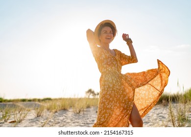 stylish attractive slim smiling woman on beach in summer style fashion trend outfit carefree and happy, feeling freedom, wearing yellow printed dress boho style chic and straw hat - Shutterstock ID 2154167315