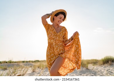 Stylish Attractive Slim Smiling Woman On Beach In Summer Style Fashion Trend Outfit Carefree And Happy, Feeling Freedom, Wearing Yellow Printed Dress Boho Style Chic And Straw Hat