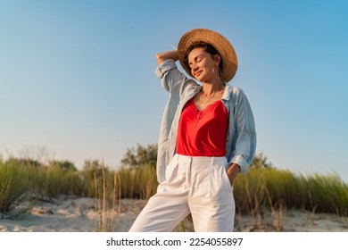 stylish attractive slim smiling woman on beach in summer style fashion trend outfit happy having fun wearing white pants red top blue shirt boho style chic and straw hat - Powered by Shutterstock