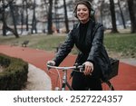 A stylish and attractive young businesswoman wearing headphones while riding a bicycle in an urban park setting, exuding confidence and joy.