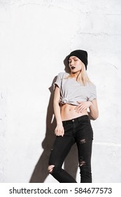 Stylish attractive young woman in hat and torn jeans with black makeup over white background