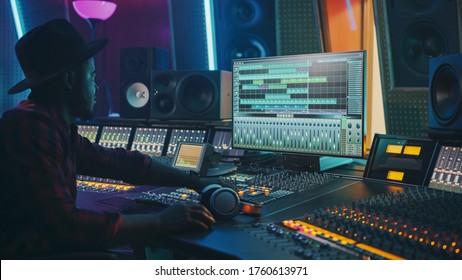 Stylish Audio Engineer Working in Music Recording Studio, Uses Mixing Board and Software to Create Modern Hit Song. Portrait of Black Artist Musician Working at Control Desk - Powered by Shutterstock