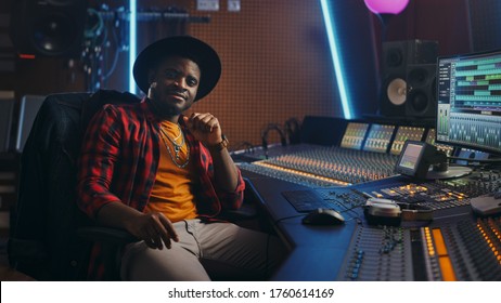 Stylish Audio Engineer Working in Music Recording Studio, Uses Mixing Board and Software to Create Modern Hit Song. Looking at Camera Portrait of Black Artist Musician Working at Control Desk - Powered by Shutterstock