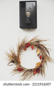 Stylish Autumn Wreath Hanging At Modern Lantern On White Wall Outdoor. Fall Decor And Arrangement Of Farmhouse Exterior. Rustic Autumn Wreath With Dried Grass, Berries, Herbs And Leaves