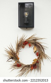 Stylish Autumn Wreath Hanging At Modern Lantern On White Wall Outdoor. Fall Decor And Arrangement Of Farmhouse Exterior. Rustic Autumn Wreath With Dried Grass, Berries, Herbs And Leaves