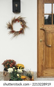 Stylish Autumn Wreath Hanging At Modern Lantern, Pumpkins And Flowers At Wooden Door Outdoor. Fall Decor And Arrangement Of Farmhouse Exterior. Rustic Autumn Decoration