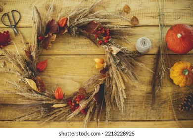 Stylish autumn wreath on rustic table flat lay. Rustic autumn wreath with dried grass, berries, herbs on wooden table with candle, scissors and pumpkins. Fall decor and arrangement in farmhouse.