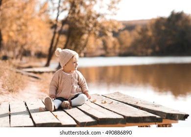 Stylish Baby Girl 1 Year Old Wearing Knitted Autumn Clothes Sitting In Park. Looking Away. Childhood. 