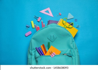 Stylish backpack with different school stationary on blue background, top view