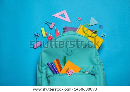 Stylish backpack with different school stationary on blue background, top view
