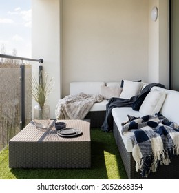 Stylish balcony with fake grass and comfortable, rattan corner sofa with pillows and blankets and square coffee table