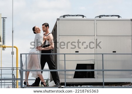 Stylish ballroom dancers performing choreography near railing on roof of building outdoors 