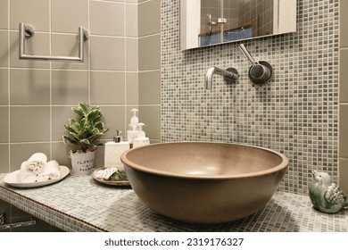 Stylish bathroom design. Modern sink bowl on the countertop decorated with mosaic tiles. Hygiene products, towels, potted houseplant.