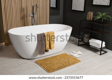 Stylish bathroom interior with bath tub, houseplant and soft yellow mat