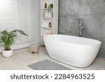 Stylish bathroom interior with ceramic tub, care products and towels in cabinet