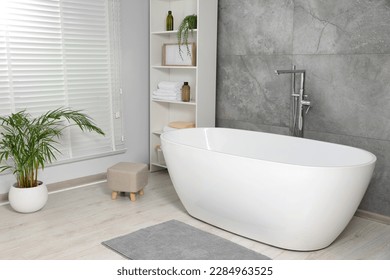 Stylish bathroom interior with ceramic tub, care products and towels in cabinet - Shutterstock ID 2284963525