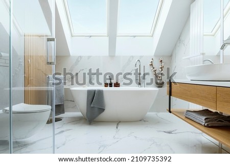 Stylish bathroom interior design with marble panels. Bathtub, towels and other personal bathroom accessories. Modern glamour interior concept. Roof window. Template.