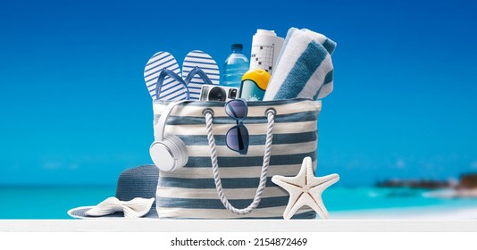 Stylish beach bag with accessories and tropical beach in the background, summer vacations concept - Shutterstock ID 2154872469