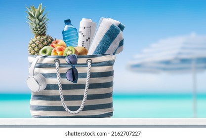 Stylish beach bag with accessories and tropical beach in the background, summer vacations concept - Powered by Shutterstock