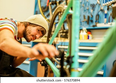 Stylish Bearded Bicycle Mechanic Doing His Professional Work In Workshop - Young Trendy Man Checking New Carbon Fiber Racing Bike Indoor - Repairing Bikes Concept -  Focus On His Face - Warm Filter