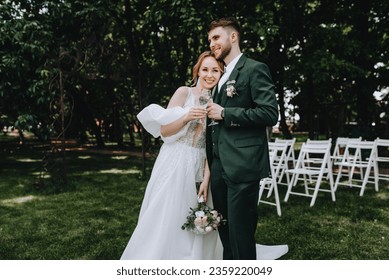 A stylish bearded groom and a beautiful smiling bride in a white dress are hugging, holding glasses of champagne in their hands. Wedding photography of newlyweds, portrait, lifestyle. - Powered by Shutterstock