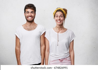 Stylish Bearded Male In T-shirt And Cute Female With Yellow Headband Smiling Unnaturally Showing Thier White Perfect Teeth Posing Against White Background. People, Emotions And Lifestyle Concept