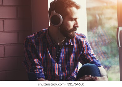 Stylish Bearded Man  In Headphones Listening To Music Near Window With Reflection