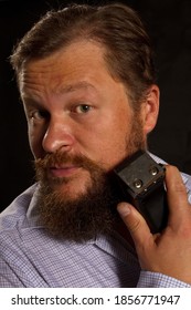 Stylish Bearded Man Shaving By Electric Razor Studio Portrait On Black Background.