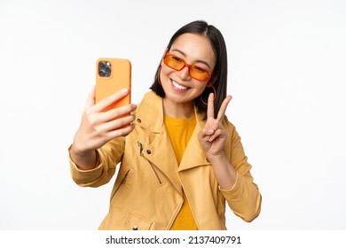 Stylish, Beautiful Asian Girl In Sunglasses, Taking Selfie On Smartphone, Posing For Photo, Holding Mobile Phone, White Studio Background