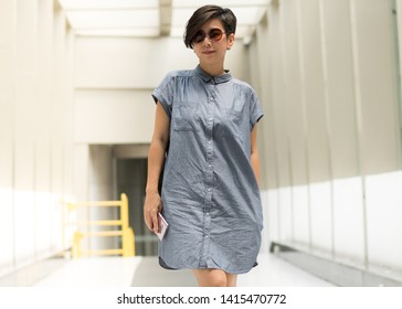 A Stylish Beautiful Asian Woman Walking In The Open Air Walk Way. She's Wearing UV Protection Sun Glasses And Have A Smart Phone In Her Hand. Sun Light, UVA-UVB.