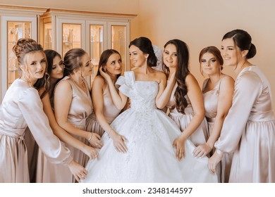 Stylish beautiful bridesmaids in matching silk dresses helping gorgeous brunette bride in white dress get ready for wedding, morning preparations, woman putting on dress - Powered by Shutterstock