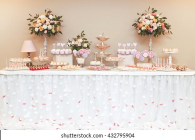 Stylish beautiful luxury sweet candy bar set  on the table at the wedding ceremony in restaurant. Flower rose bouquet and tasty desserts on the table. Confectionery business concept.
