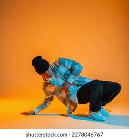 Stylish beautiful professional dancer in trendy fashion clothes with a shirt, hat, jeans and white sneakers dances on the floor in a creative color studio with orange and neon lights - Shutterstock ID 2278046767
