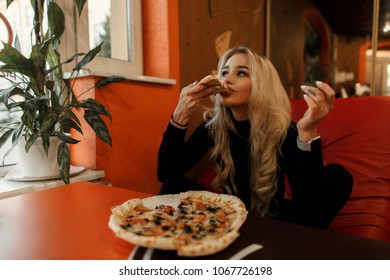 Stylish beautiful young woman eating pizza at a table in a cafe