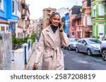 Stylish and beauty african american businesswoman wearing trench coat talking to the mobile phone in the city