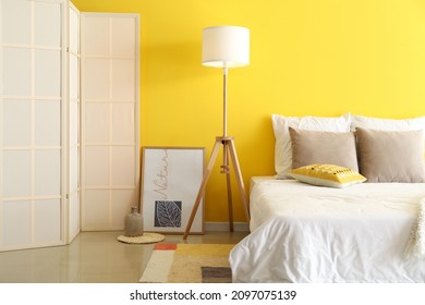 Stylish Bedroom With Comfortable Bed, Floor Lamp And Folding Screen Near Color Wall