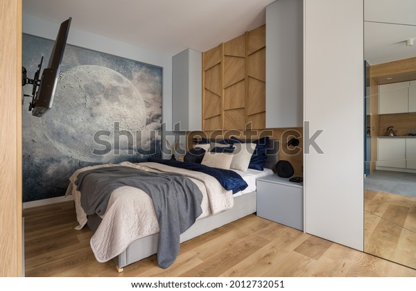 Stylish bedroom with comfortable bed, tv, wood décor and nice wallpaper with moon.