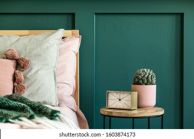 Stylish bedroom interior with design coffee table, plant, gold clock and elegant personal accessories. Beautiful bed sheets, blanket and pillows. Template. Modern home staging. Wall panelling. Details