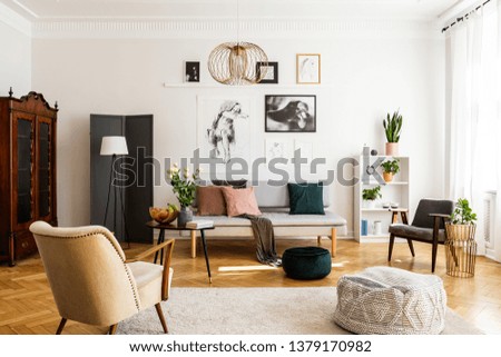 Stylish beige armchair and pouf on the cozy carpet in classy living room interior with grey settee and vintage furniture