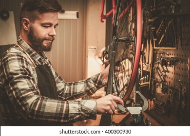 Stylish bicycle mechanic doing his professional work in workshop.