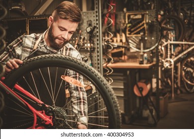 Stylish bicycle mechanic doing his professional work in workshop. 