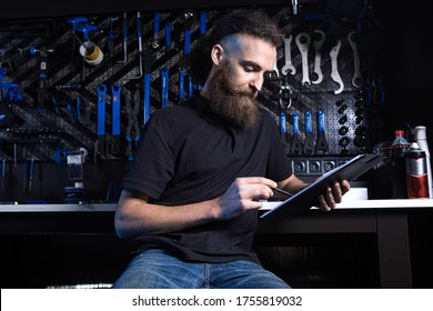 Stylish Bicycle Mechanic Making Notes In Clipboard In Workshop. Theme Small Business Selling, Repair And Service Bicycles. Technician Doing Administrative Paperwork In Bike Shop. Manage Business.