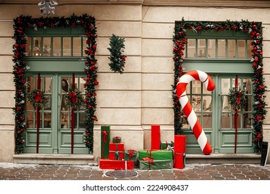 Stylish big candy cane, red and green wrapped christmas gifts, fir branches, wreaths on building exterior. Modern christmas decor in city street. Winter holidays in Europe. Merry Christmas