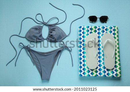 Stylish bikini and beach accessories on light blue background, flat lay