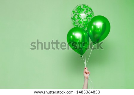 stylish birthday party or holidays with colorful  balloons close up. green  balloons isolated on the green  background with copy space for text. Hand  holding three bright colorful balloons indoor.