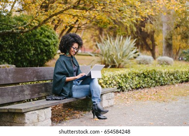 Stylish Black Female Entrepreneur Working With Modern Convertible Laptop Outdoor In Autumn At City Park. Young Professional Woman Outside Using Tablet.