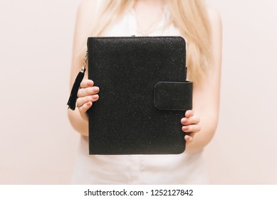 Stylish black notebook with a brush and a button in the hands of the girl. Free space for logo